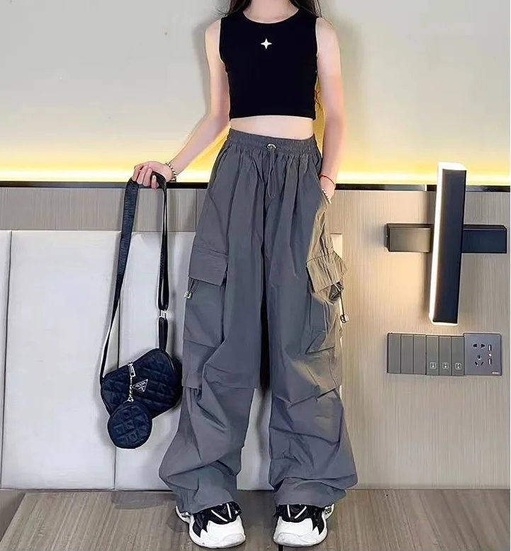 Teen girl posing in high-waisted cargo joggers with a vintage streetwear look, standing against a graffiti wall gray