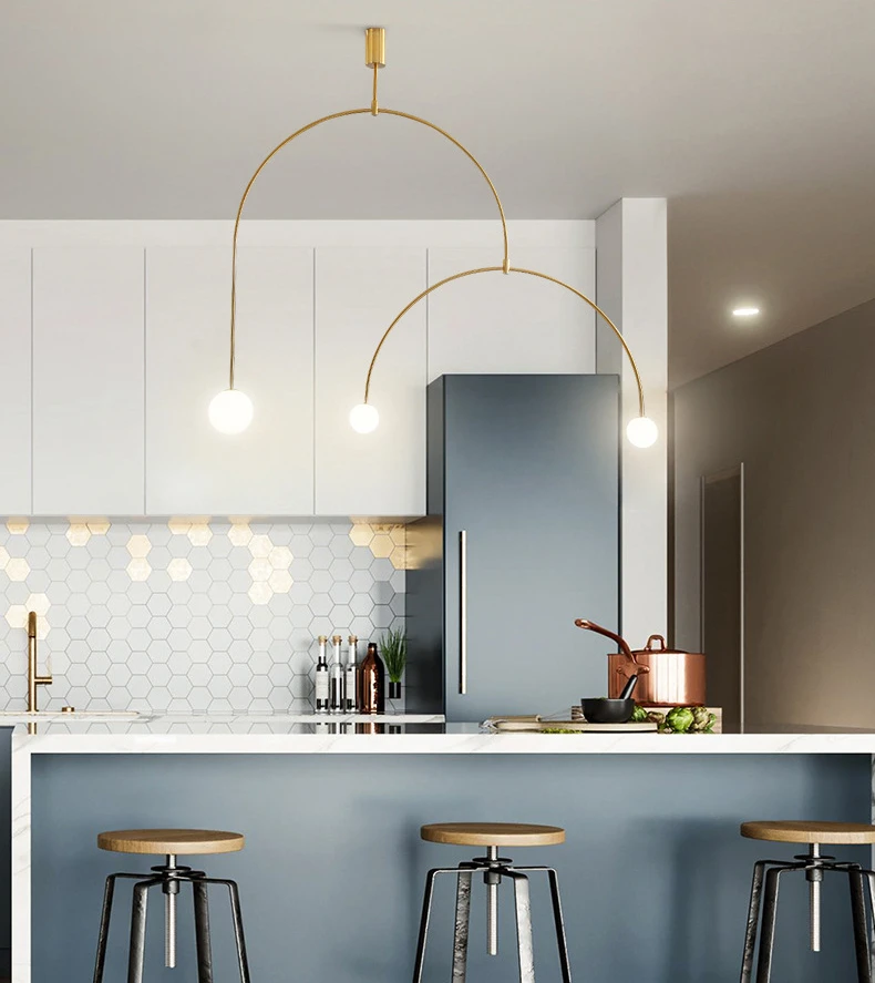 A modern kitchen with a white island, three wooden stools, hexagonal tile backsplash, and the Minimalist Line Light featuring a gold arc-shaped pendant that enhances clean lines and elegance.