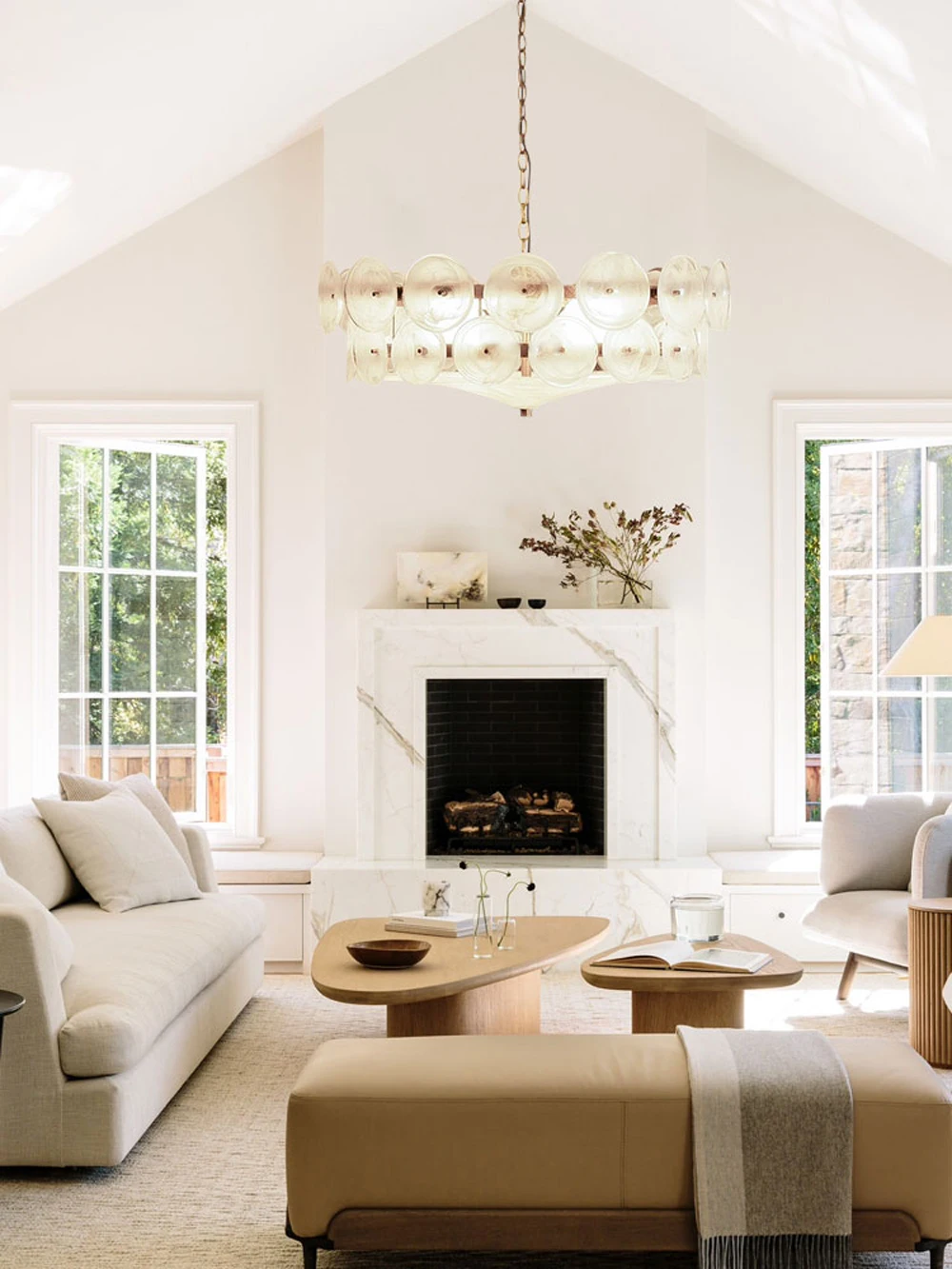 Bright living room with cream furniture, a marble fireplace, two large windows, light wood tables, neutral decor accents, and an Italian Retro Pendant Light as the central chandelier.