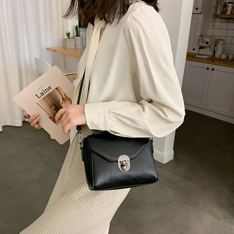 Naine kannab stiilset musta crossbody kotti sangaga, mis sobitub tema heleda riietusega. Koti minimalistlik disain sobib ideaalselt kaasaegsesse interjööri.