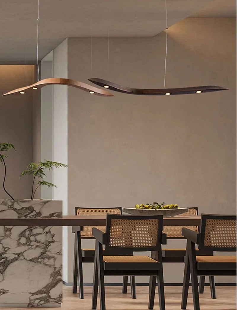 A modern dining area features a marble counter, wooden chairs with woven backs, a table with a fruit bowl, and two Spiral Wood Pendant Lights hanging from the ceiling.