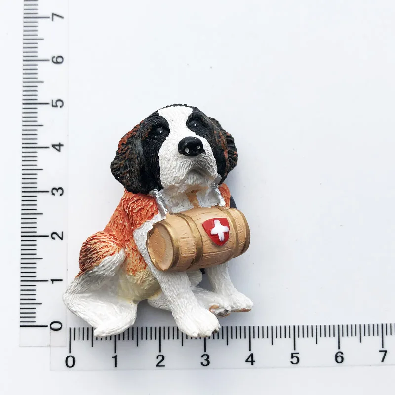 3D resin Switzerland fridge magnet featuring a detailed Saint Bernard dog sculpture holding a small wooden barrel with a white cross, displayed next to a collection of colorful Swiss travel souvenirs.