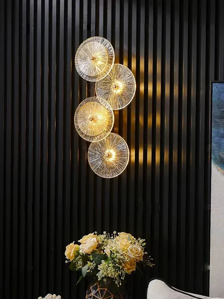 Four Amber Deco Wall Sconces with a glass disc design cast warm light on a black vertical paneled wall above a table with a floral arrangement.