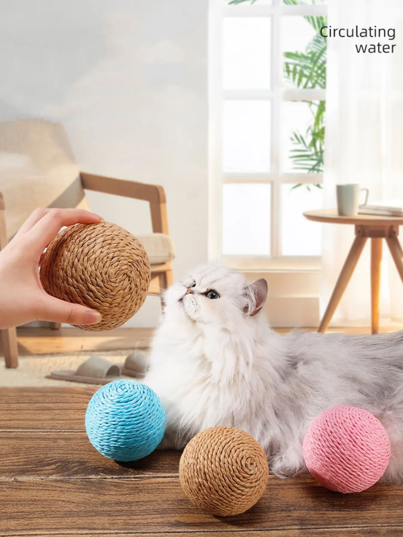 A fluffy white cat eyes the KittyNook Cat Co. Premium Sisal Kitten Scratching Ball—a playful furniture protector!.
