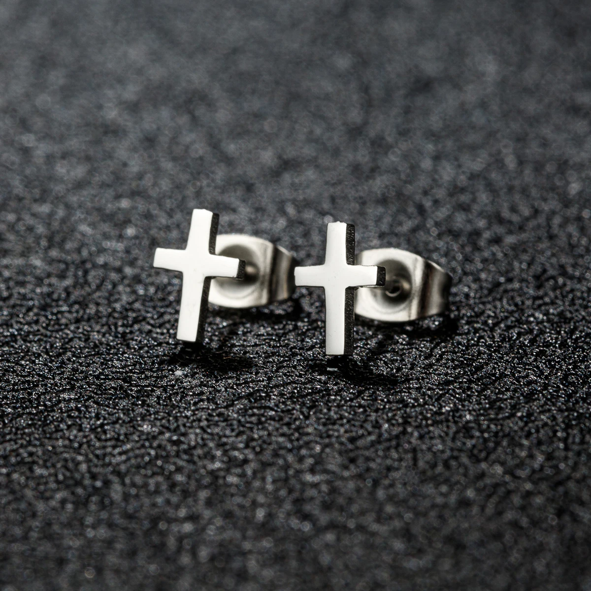 Pair of stainless steel cross stud earrings in silver tone, displayed on a textured black surface.