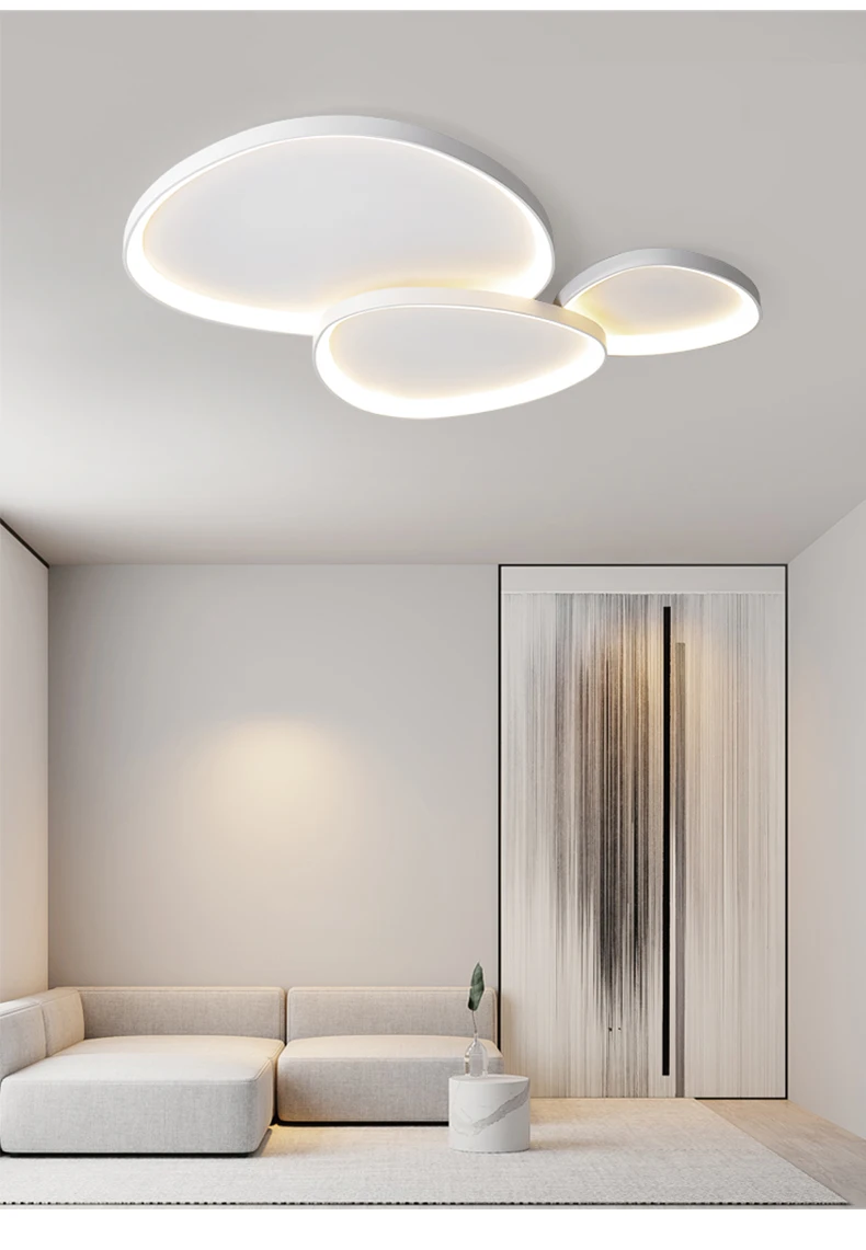 A modern minimalist living room features a white sectional sofa, round coffee table, abstract wall art, and the Nordic Minimalist Ceiling Light with dimmable brightness and color temperature control in three overlapping circular designs.