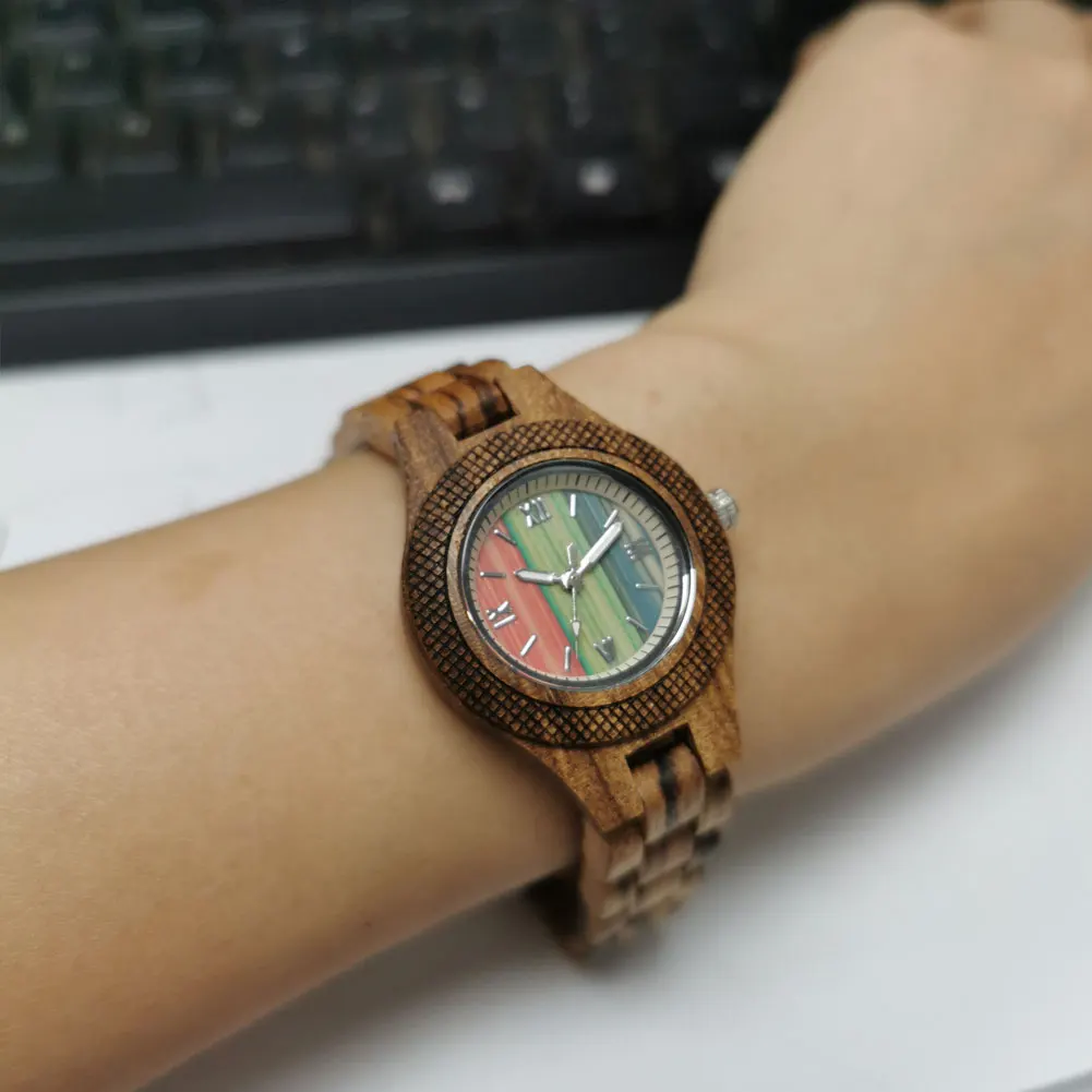 Puidust käekell naistele pruuni puidust rihmaga ja värvilise sihverplaadiga randmel, mille taustal on klaviatuur.