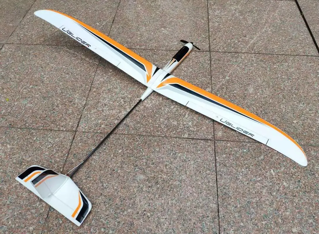 Planeur RC U-GLIDER 300g posé sur l'herbe, ailes repliées, mettant en avant sa structure légère et son moteur 2208.