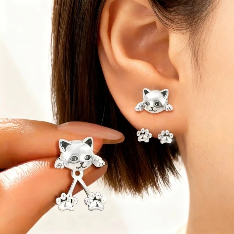 A person wears KittyNook Cat Co. Vintage Silver Cat Back-Hanging Earrings with dangling paws and kitten silhouette.