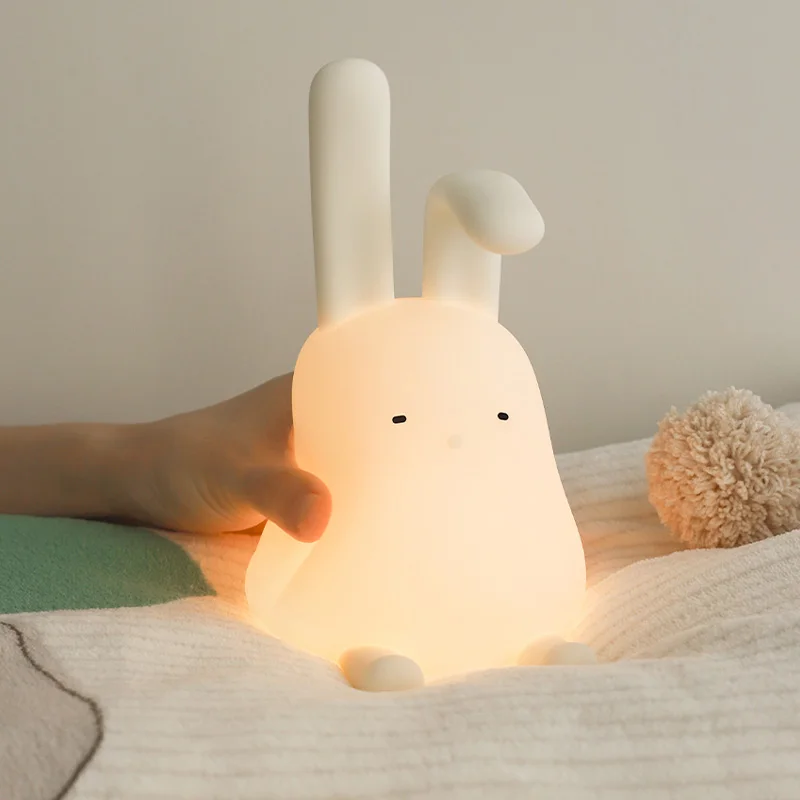 A creative and adorable person holding a Bunny Touch Lamp night light on a bed.