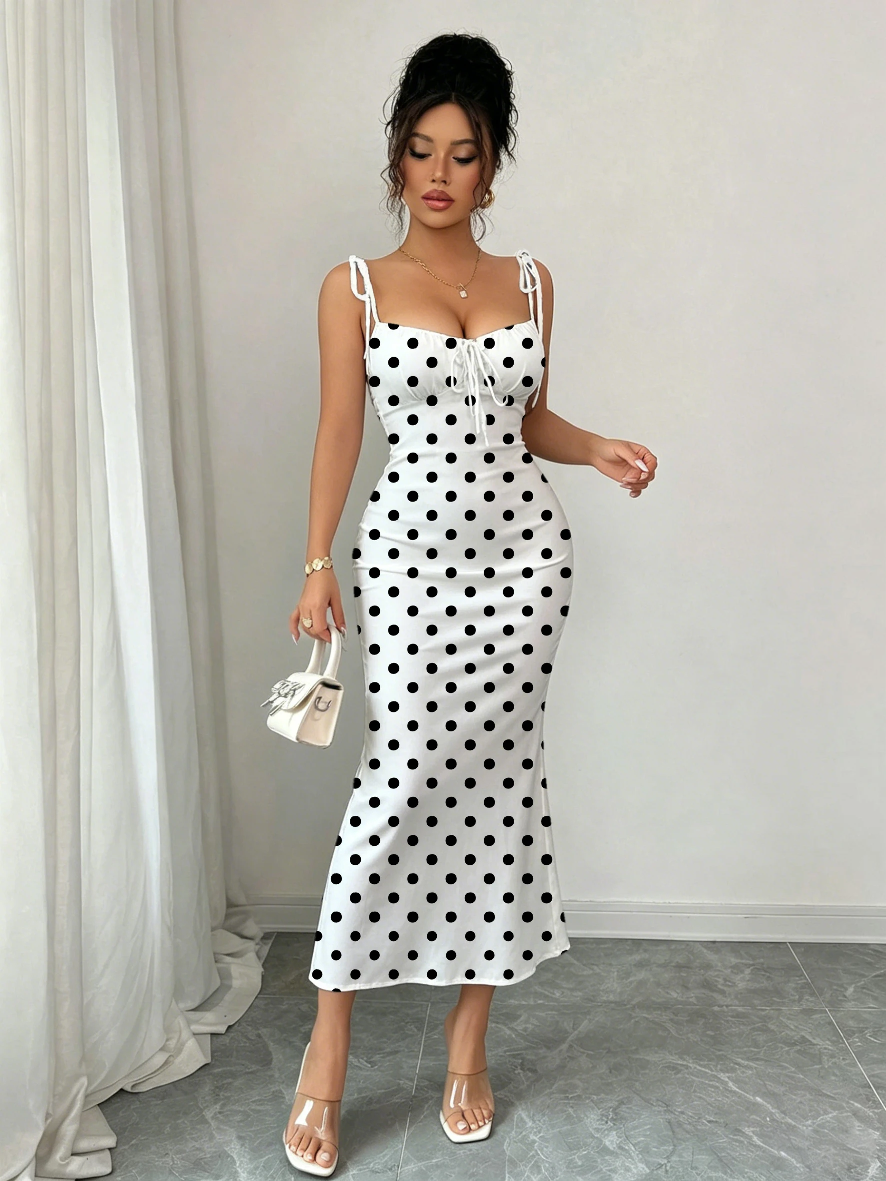 Robe sirène noire à pois sur fond blanc, avec double nœud papillon aux épaules et fronces sur la poitrine pour une mise en valeur de la taille, coupe ajustée, moulante aux hanches, longueur mi-longue