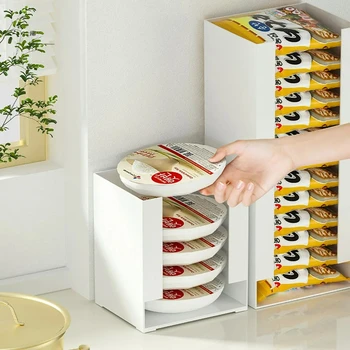 A white and clear instant noodle storage box sitting on a kitchen counter, neatly filled with packets of Korean ramen.
