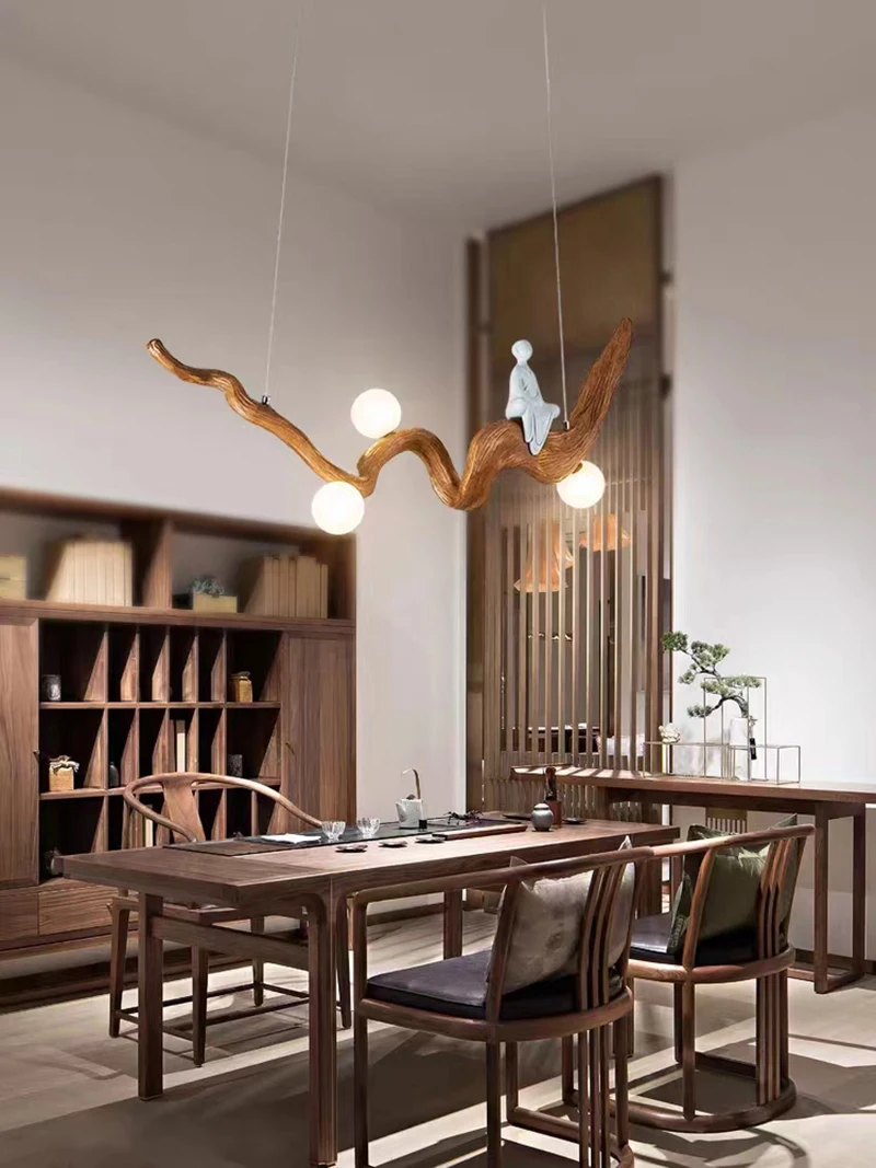 A modern dining room with wooden furniture highlights organic beauty, featuring the Zen-Inspired Wooden Pendant Light, resembling a twisted branch with glowing bulbs and a small decorative figure.