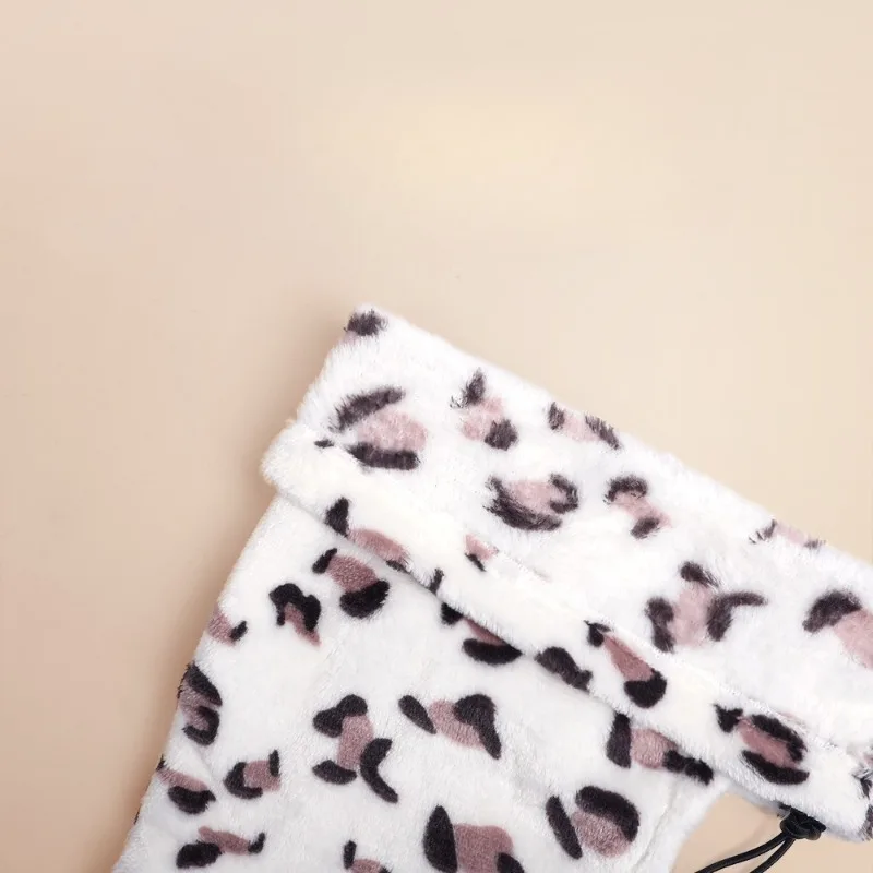 Close-up detail of a plush, leopard-print fleece dog accessory. The fabric shows a white base with soft brown and black spots, highlighting the thick, warm material and the elastic drawstring cord at the bottom.