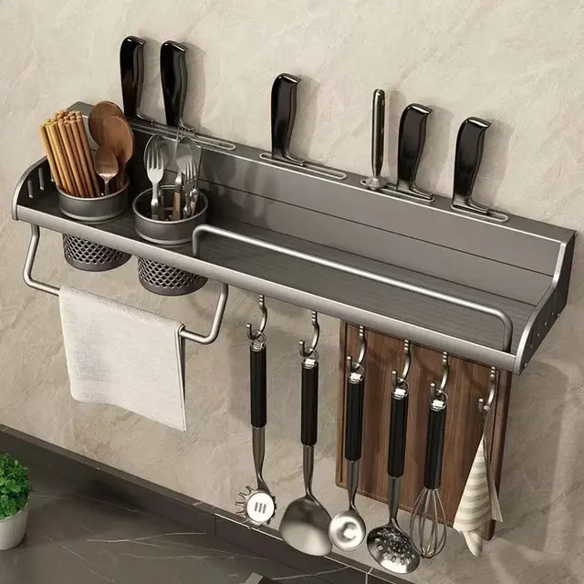 A black, aluminum wall mounted kitchen rack holding spices, knives, and utensils above a clean, modern kitchen counter.