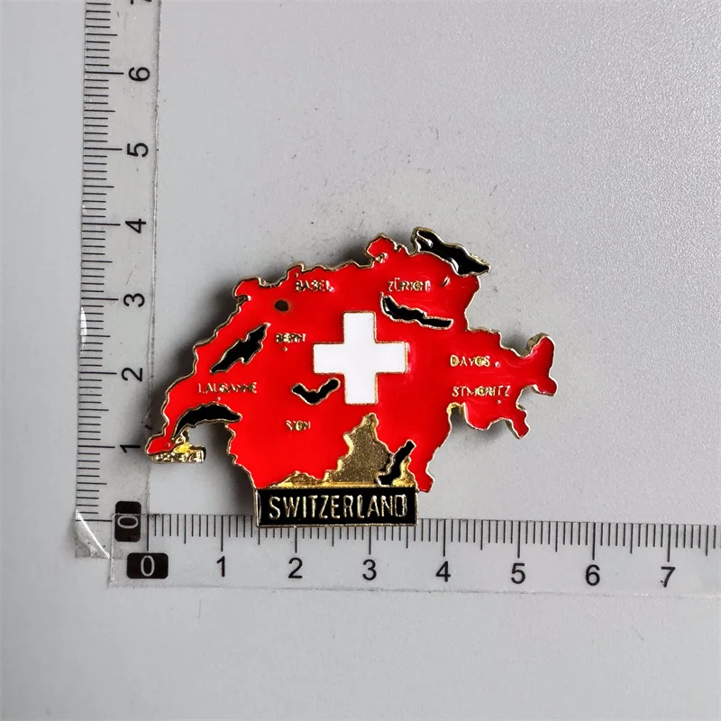 3D resin Switzerland fridge magnet featuring a detailed Saint Bernard dog sculpture holding a small wooden barrel with a white cross, displayed next to a collection of colorful Swiss travel souvenirs.