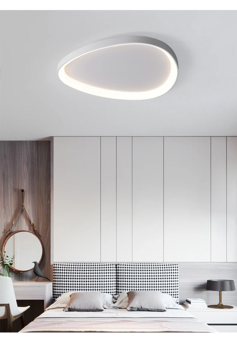 A modern bedroom showcases the Nordic Minimalist Ceiling Light, offering dimmable brightness and color temperature control. The white and wood panel walls highlight a neatly made bed with two pillows, while a round mirror, lamp, and chair add style and comfort to the space.