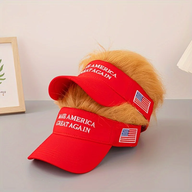 Two "Visor Cap - Make America Great Again" satirical caps with embroidered slogans, attached fake blond hair, and small American flag patches are stacked on a gray surface—perfect for sparking patriotic conversation.