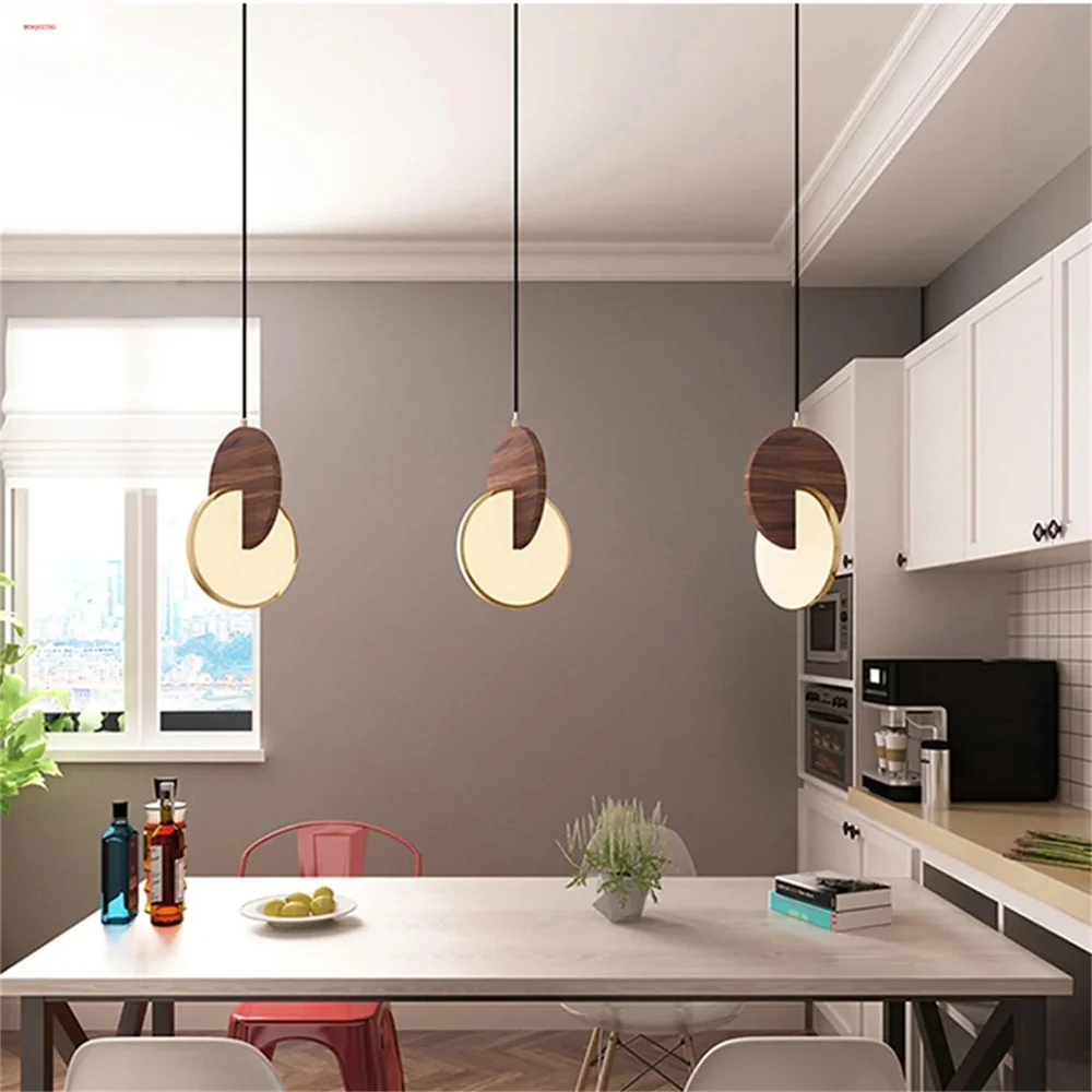 A modern kitchen with a white table under the Dual Disc Pendant Light and a vibrant red chair surrounded by lush plants. Sleek white cabinets and appliances enhance the sophisticated home aesthetic.