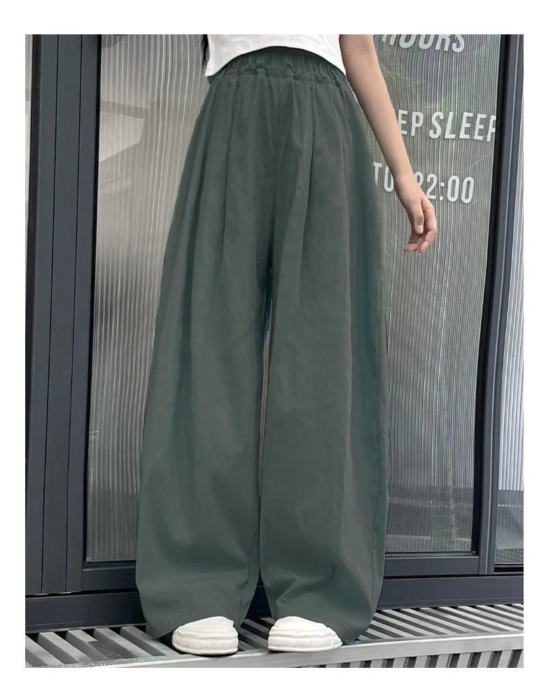 Teen girls’ casual summer wide-leg pants in lightweight fabric, styled with sandals and a simple tee on a beach boardwalk backdrop green