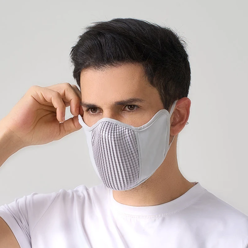 Masque de protection solaire UPF50+ noir et gris porté par une personne de face, avec un arrière-plan flou de plage.