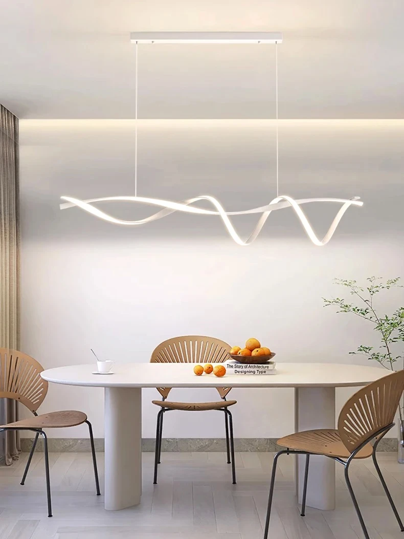 A modern dining room showcases an elegant design with a Stylish Pendant Light featuring curvy, wave-like lines above an oval table holding oranges, a book, and two decorative chairs. Neutral walls and a small plant complete the scene.