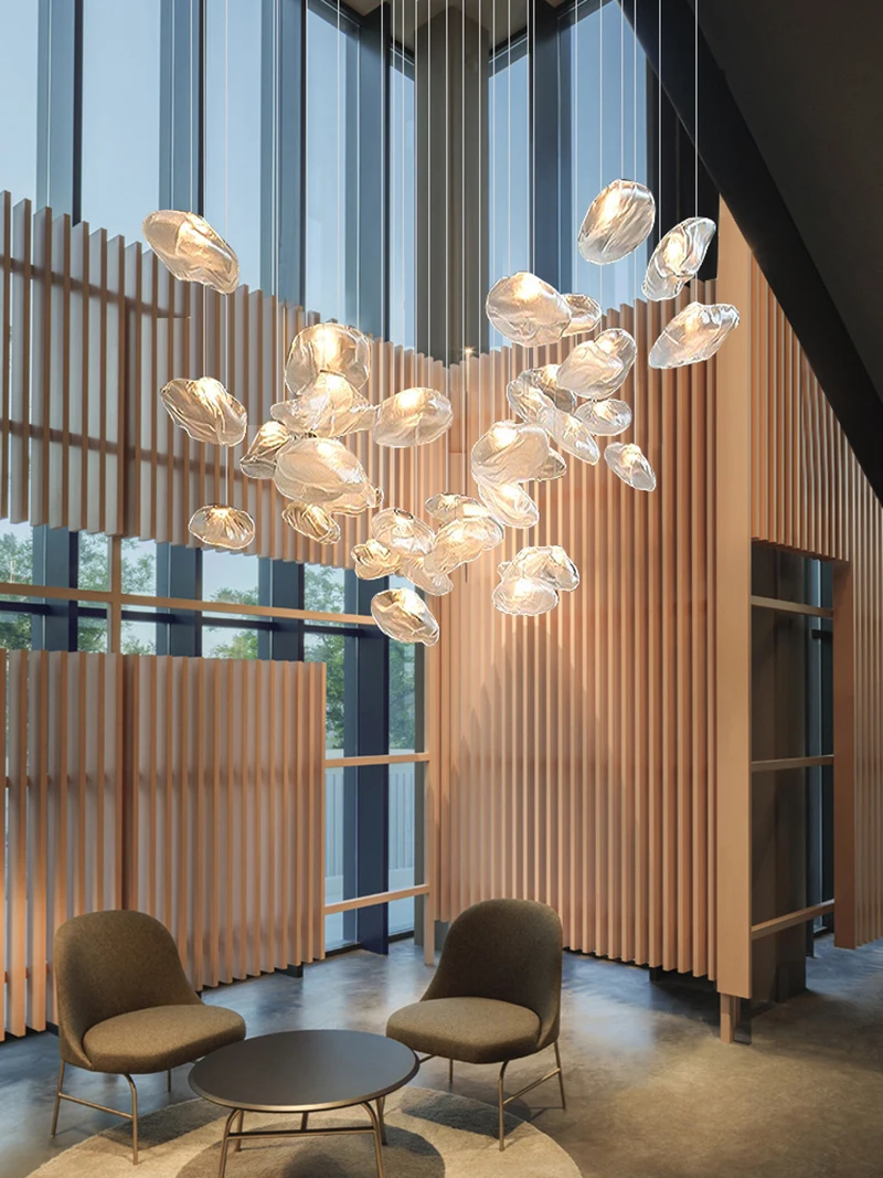 Modern lobby with tall windows, wooden slat walls, two armchairs, a round table, and the Luxe Cloud Glass Pendant Light—a sculptural hanging lamp featuring textured glass elements.