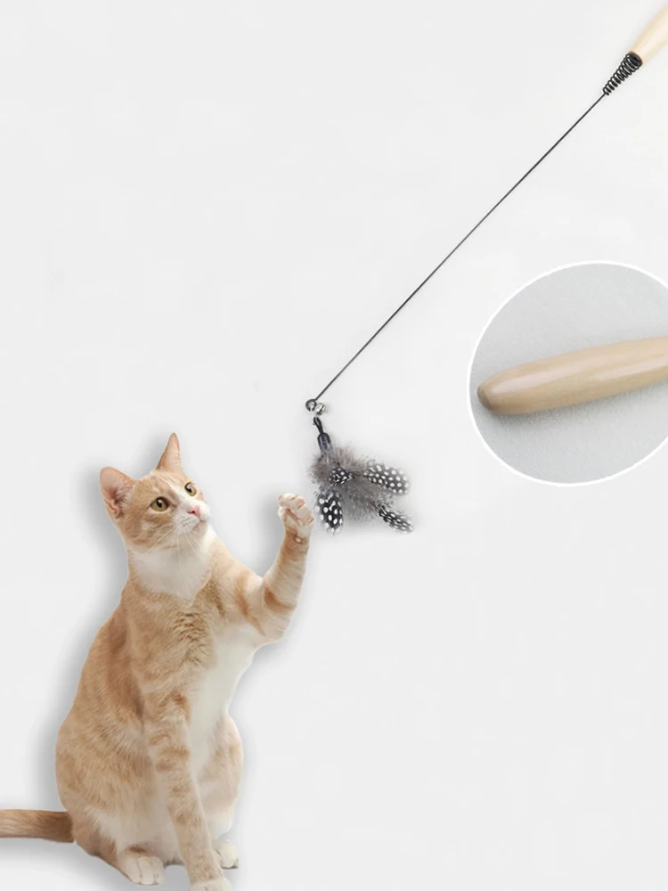 A light orange cat plays with the KittyNook Cat Co. Eco-Friendly Wood & Feather Cat Teaser against a plain background.