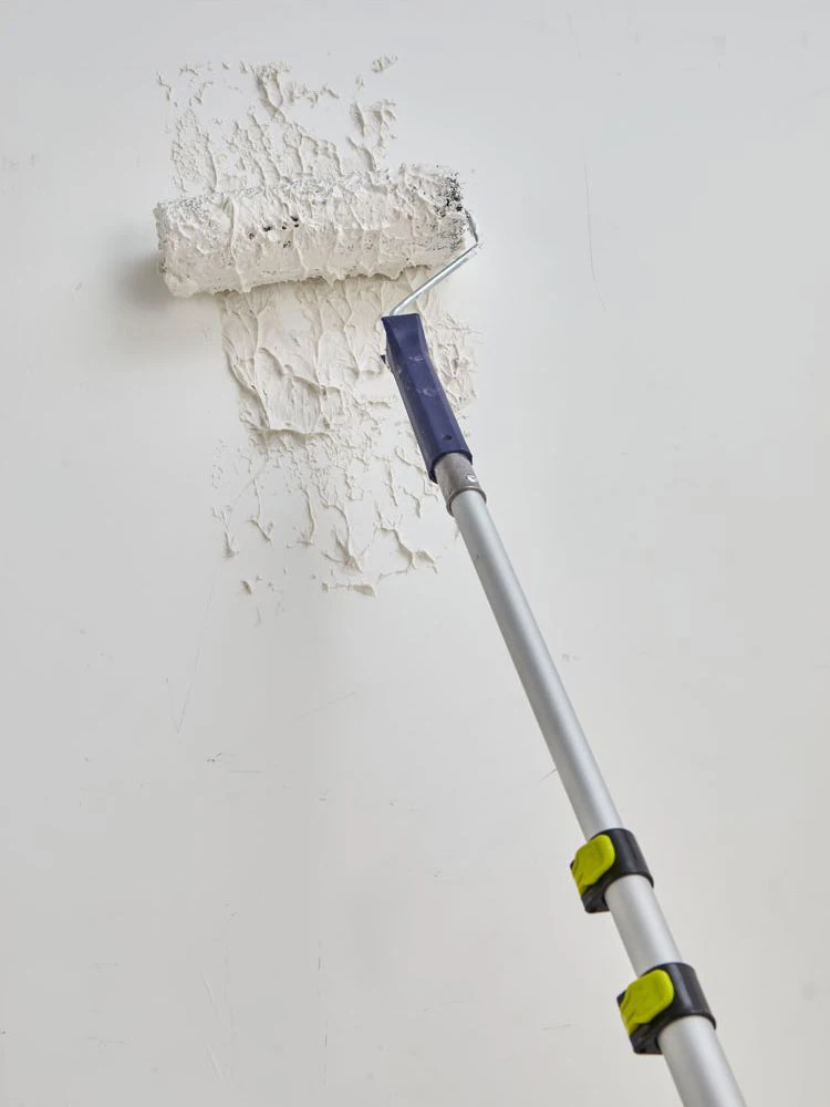 Rouleau-peinture-poignee-bleue-avec-perche-etale-platre-sur-mur-gris