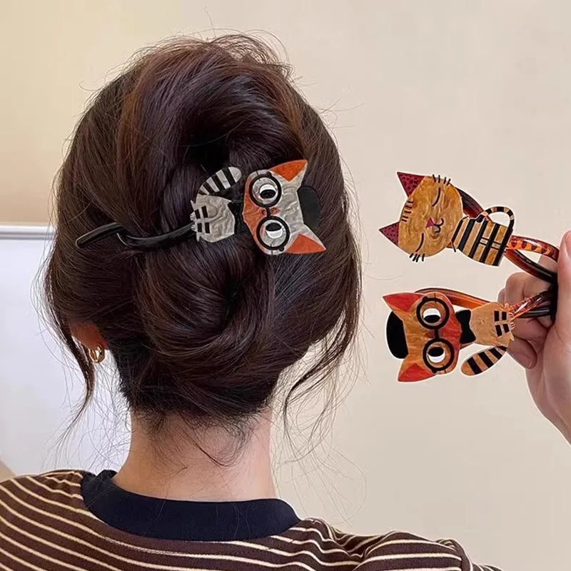 A woman with a bun holds two KittyNook Cat Co. Acrylic Cat Hairpins and wears another in her hair.