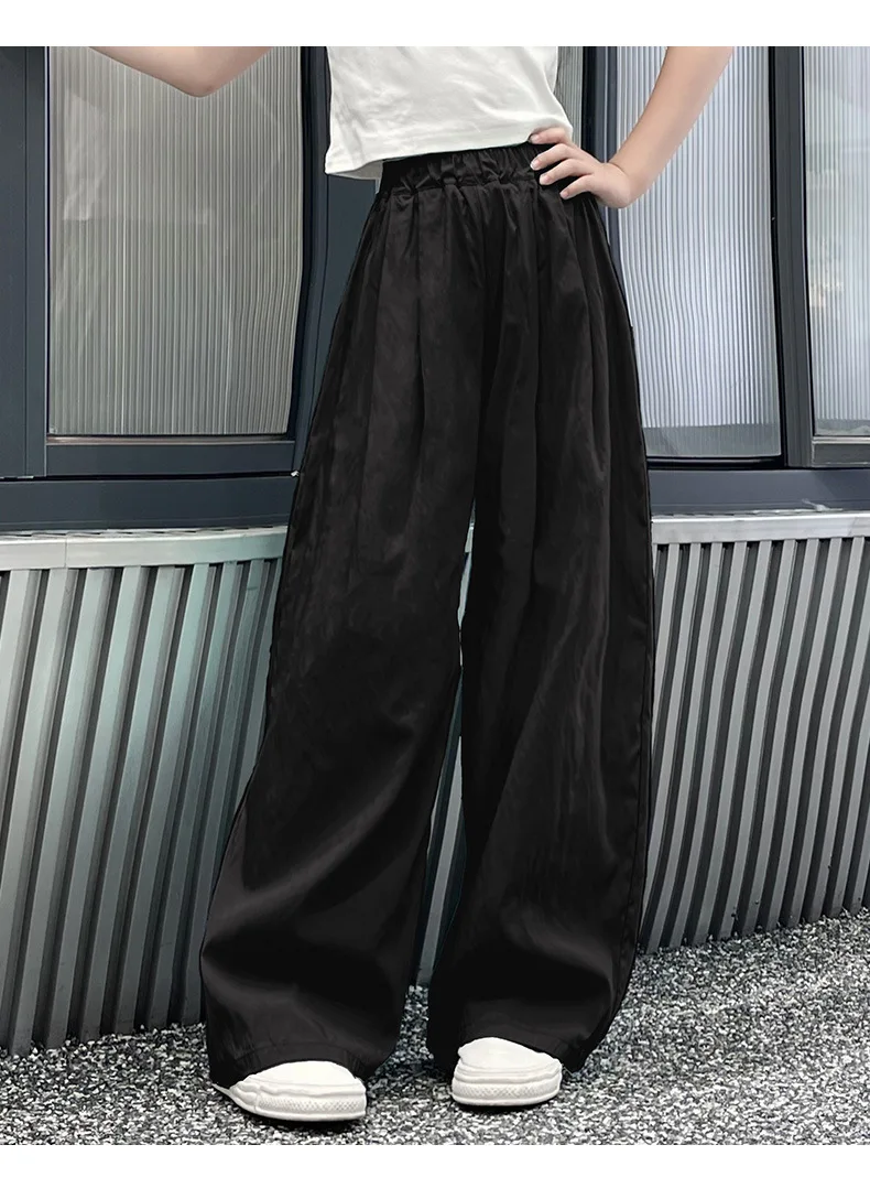 Teen girls’ casual summer wide-leg pants in lightweight fabric, styled with sandals and a simple tee on a beach boardwalk backdrop black