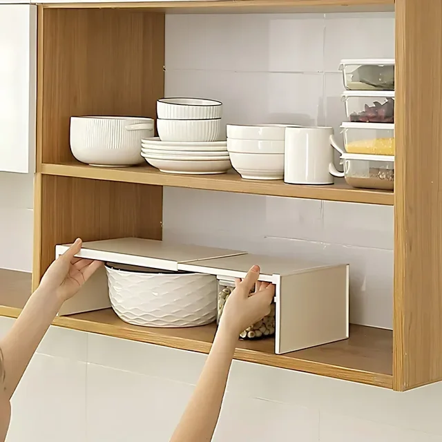 A white expandable cabinet shelf placed inside a kitchen cabinet, creating a second layer for stacking mugs and bowls.