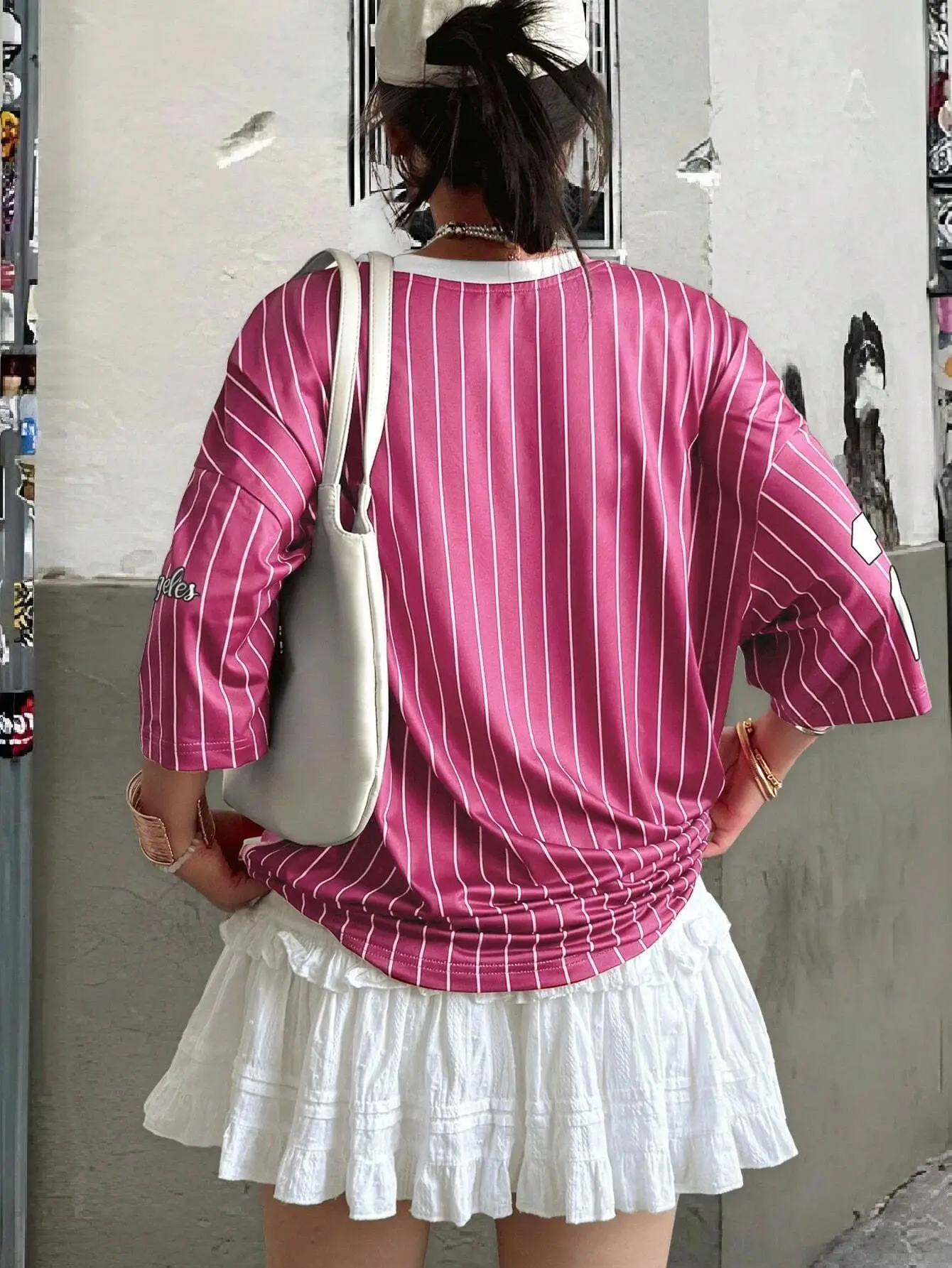 Man and woman wearing matching short-sleeved V-neck T-shirts with bold “23” digital print, standing in a sunny urban setting with sporty accessories pink back