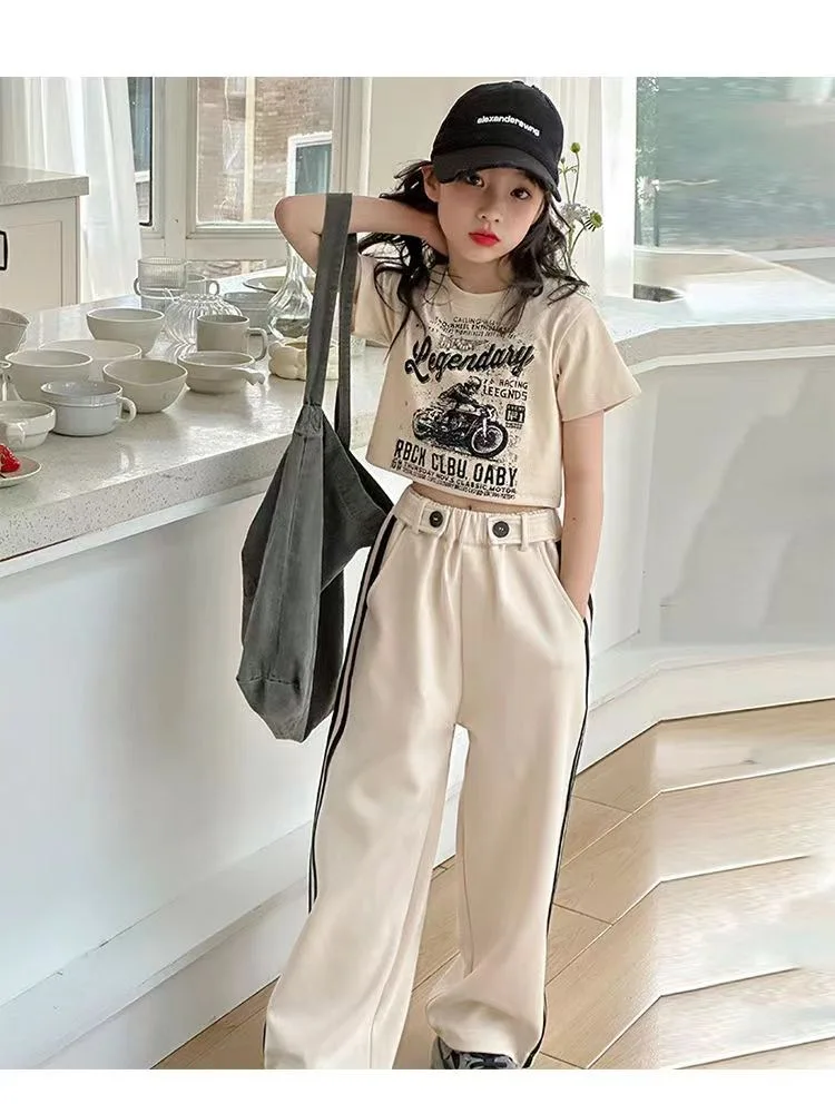 Girls’ short-sleeved T-shirt and casual pants two-piece summer set displayed on a pastel background with playful accessories beige