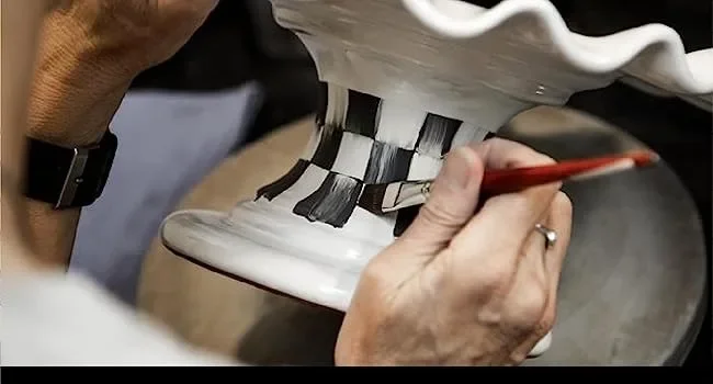 A person painting a checkered pattern on a piece of pottery.
