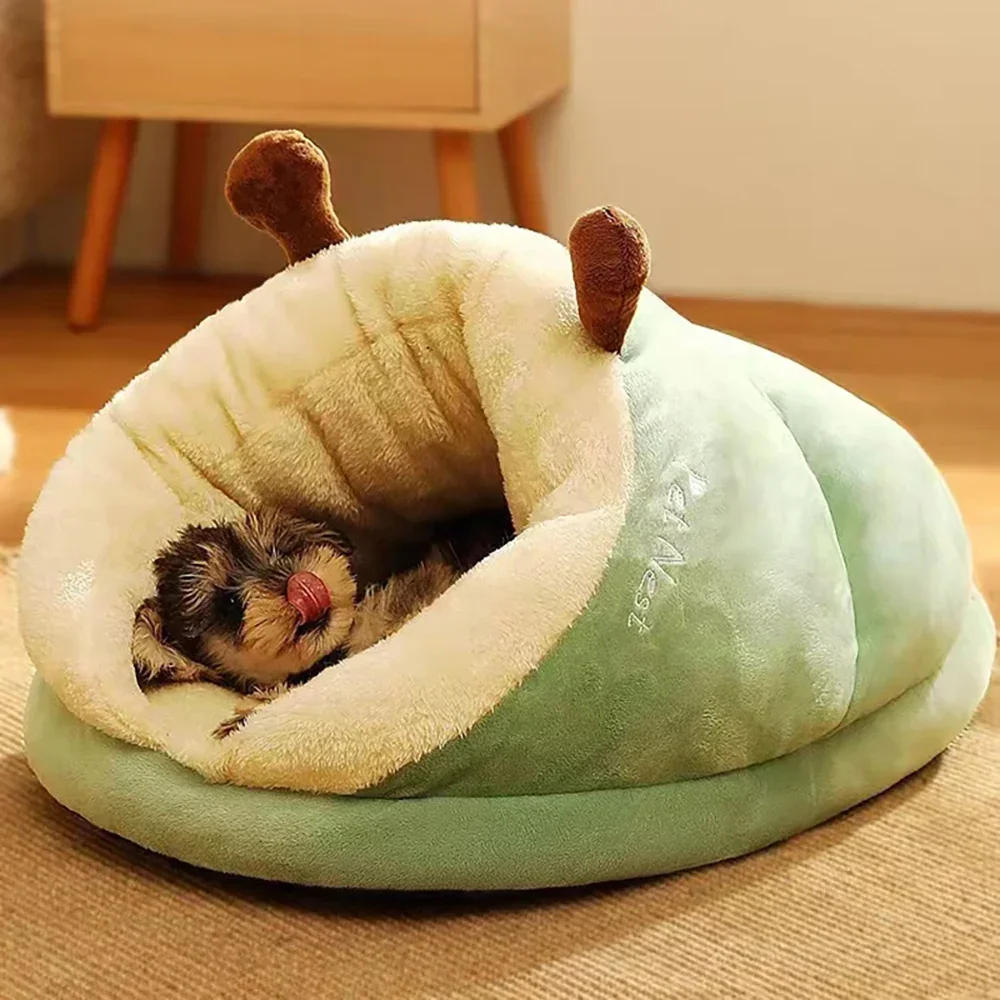 Close-up of a small puppy licking its nose while resting inside a soft, sage green hooded Warm Pet Bed.