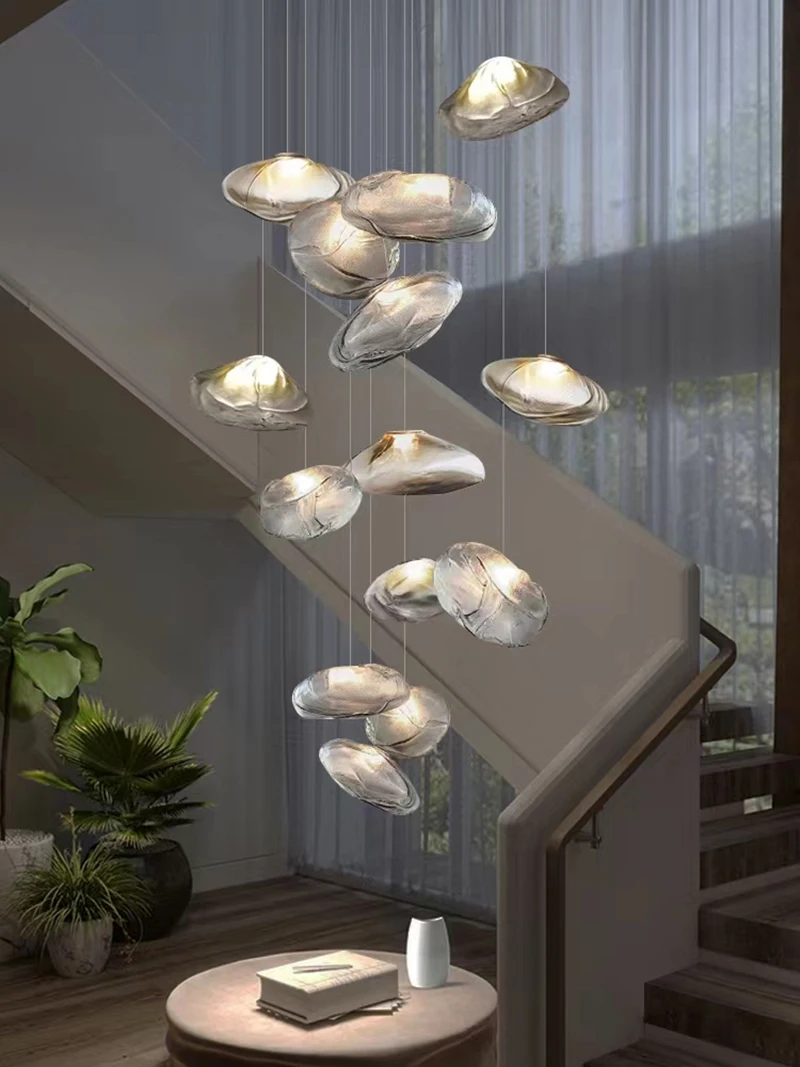 A modern staircase features Luxe Cloud Glass Pendant Lights at varying heights above a round table with a small white object, next to a potted plant.