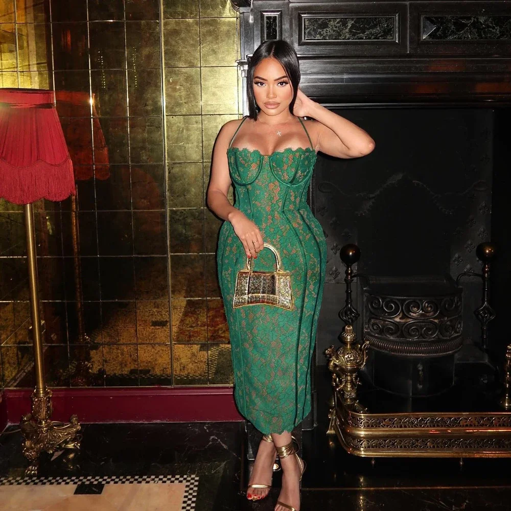 A woman wearing the Vintage Lace Dress stands in front of a dark fireplace, holding a small handbag. Beside her is a red lamp, with gold-tiled walls in the background.