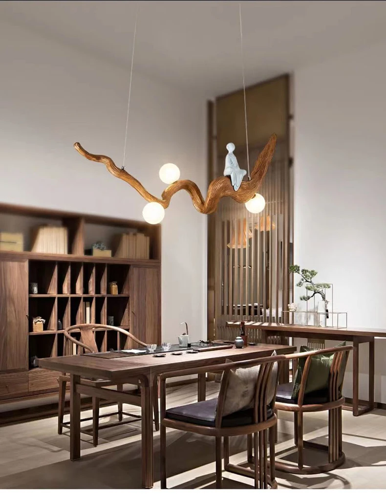 A modern dining room features a Zen-Inspired Wooden Pendant Light resembling a wooden branch with spherical bulbs, accompanied by a decorative figure. Natural wood furniture and shelves complete the minimalist decor, evoking a tranquil Zen aesthetic.