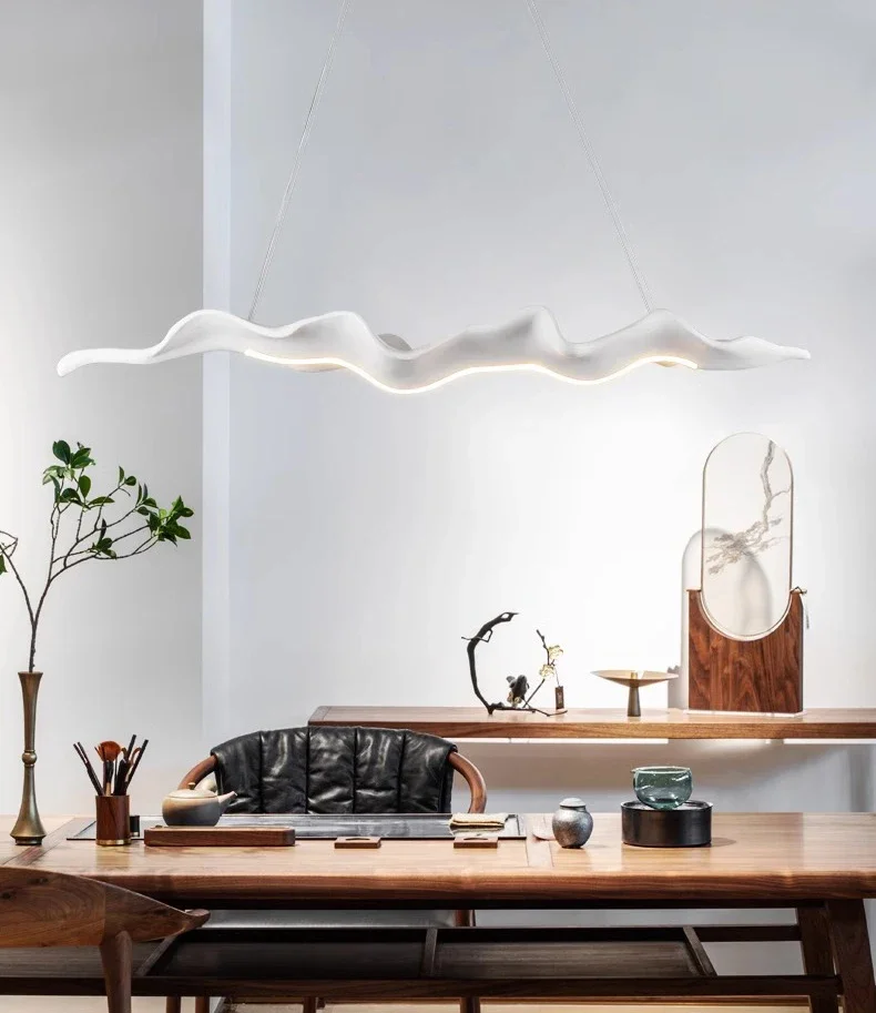 A modern dining room features the white Drift Wood Pendant Light hanging above a wooden table with chairs. Neutral beige accents harmonize seamlessly while decorative items and plants are tastefully arranged on the table and side console, infusing a natural touch into the setting.