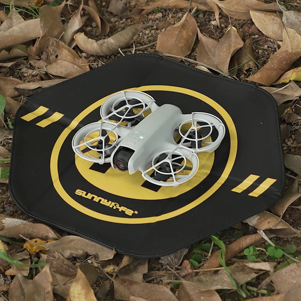 Tapis d'atterrissage pliable 35cm déplié au sol avec un drone DJI NEO posé dessus, fond neutre.