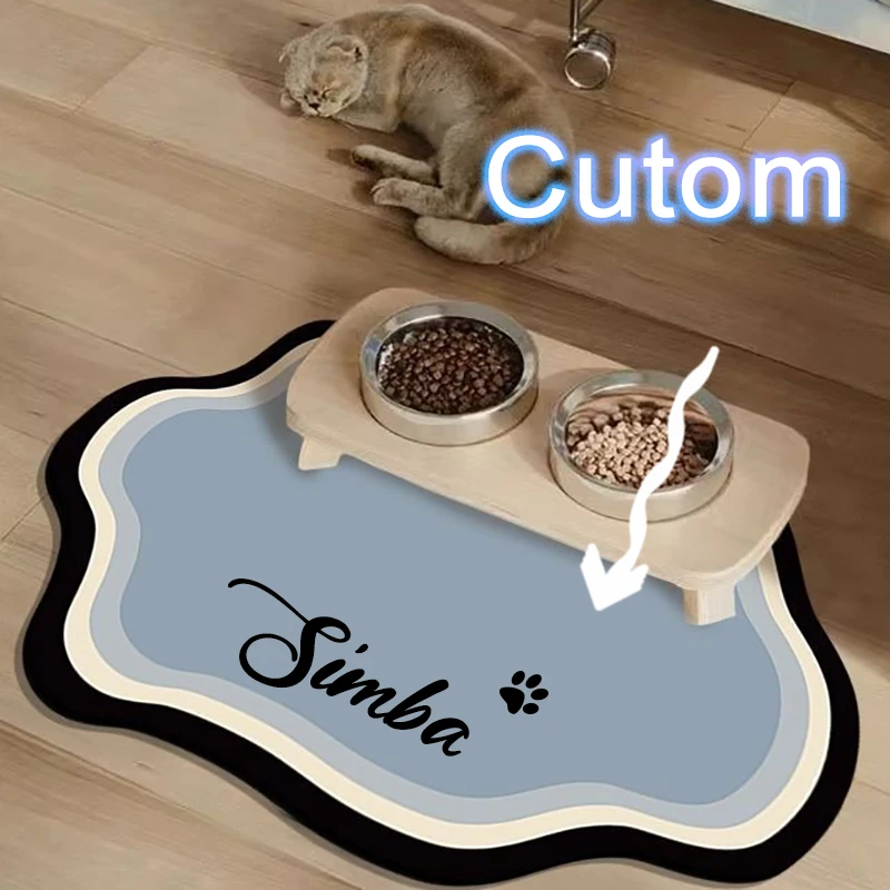 A grey cat sleeps on a wooden floor next to a light blue, wavy-edged personalized pet mat featuring the name "Simba" and a paw print.