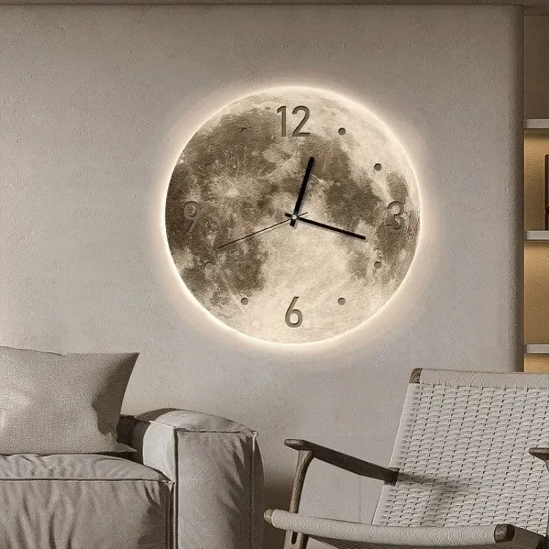 A Moon Wall Clock featuring black hour and minute hands glows softly in the dark with its lunar surface texture, hanging on a beige wall beside a white cushioned chair.