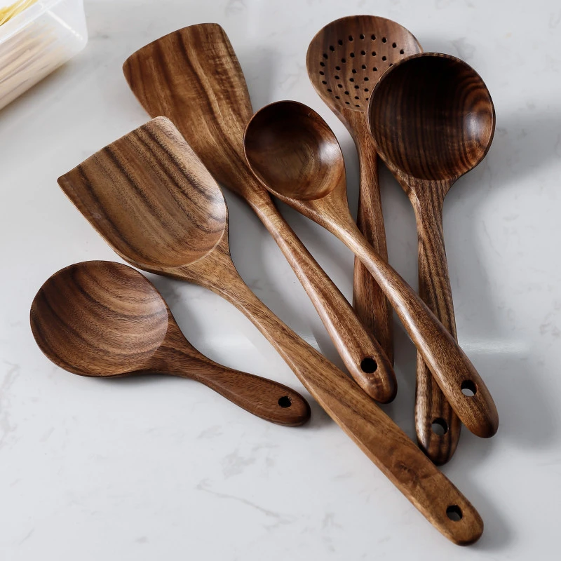 Set of natural Thailand teak wood cooking utensils including ladles, skimmers, and spoons laid out on kitchen counter 04