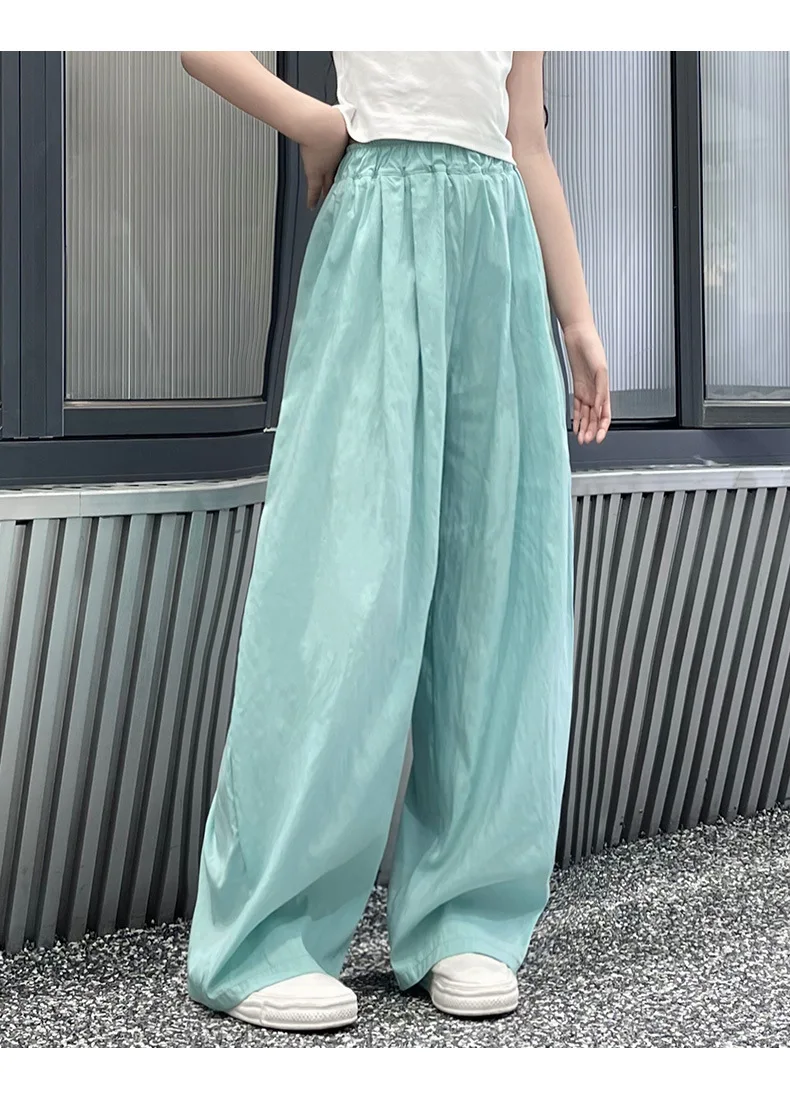 Teen girls’ casual summer wide-leg pants in lightweight fabric, styled with sandals and a simple tee on a beach boardwalk backdrop green