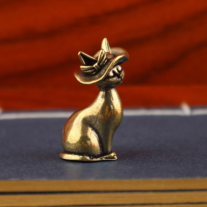 Two miniature vintage bronze cat figurines wearing elegant sunhats with ribbons, sitting on top of a book with an orange textured background.