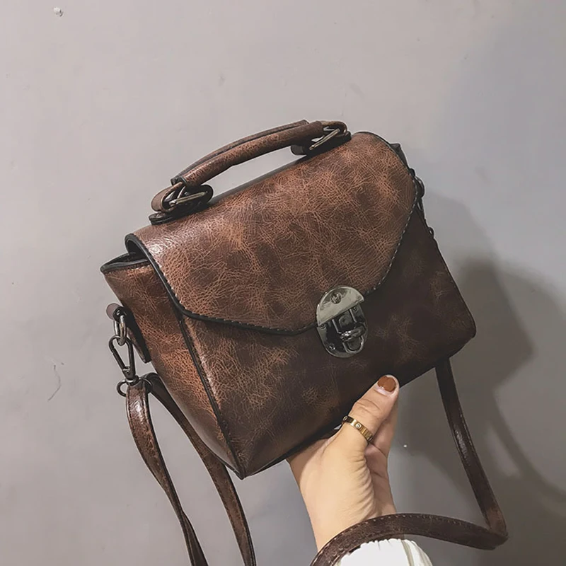Käsitsi hoitud pruun väike crossbody kott sangaga, valmistatud kvaliteetsest nahast, millel on kaunis läikiv viimistlus ja hõbedane lukk, hallil taustal.