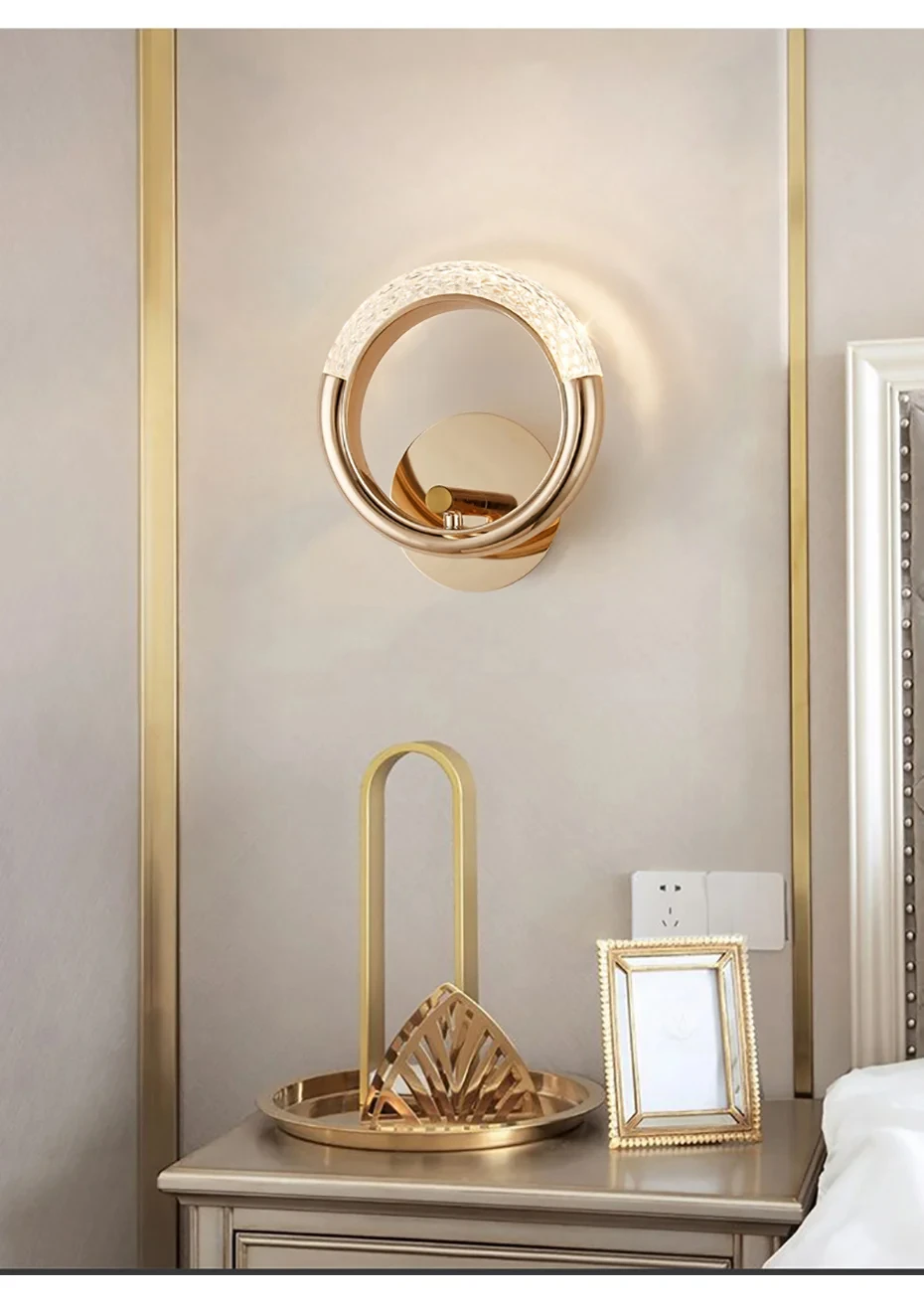 A modern and stylish bedside setup features the Luxury Wall Sconce, a gold table lamp, a framed picture, and a tray on the bedside table. The decor boasts gold accents against a neutral wall background.