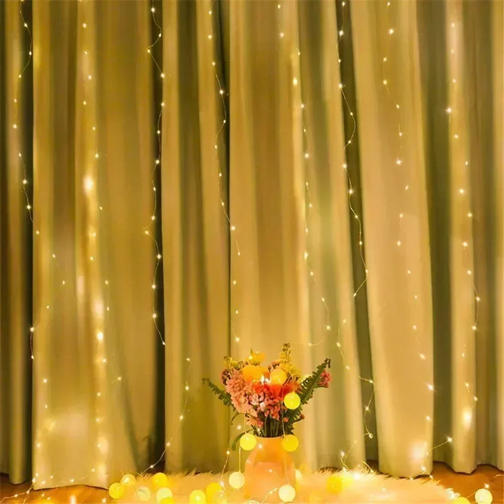 Valguskardin - 3x3 meetrit, rippumas pehme kuldse kangast tausta ees, ümbritsetuna väikestest LED-tulukestest. Ereda valgusega kardin, mis on kaunistuseks nii sise- kui välistingimustes. Põrandal on lilledega vaas ja värvilised pallid, lisades dekoratiivse elemendi.