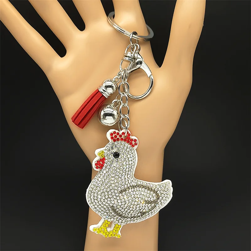 A sparkly silver rhinestone hen chicken keychain featuring a red fringe tassel and metallic bell styled on a woven straw bag and showing product dimensions in centimeters